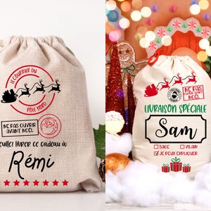 May include: Two white canvas gift bags with red and black Christmas designs. The bag on the left says "Le Courrier du Pole Nord" and "Ne pas ouvrir avant Noel". The bag on the right says "Livraison Speciale Sam" and has a checkbox that says "Je peux expliquer".