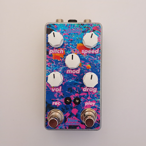 May include: A rectangular effects pedal with a colorful floral design. The pedal has six white knobs labeled "pitch", "speed", "mod", "vol", and "drag". The text "glowly" is at the top, and "flow detector" is at the bottom. Two foot switches are at the bottom.