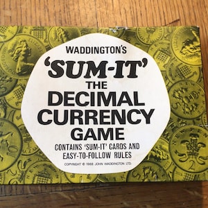 May include: A vintage board game box titled "SUM-IT The Decimal Currency Game" by Waddington's. The box is yellow with a pattern of coins and text. The game includes cards and easy-to-follow rules.