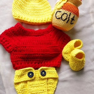 May include: A yellow and red crochet baby outfit, including a hat with ears, a shirt, diaper cover, booties, and a honey pot. The honey pot has the word "COLT" embroidered on it. The outfit is handmade.