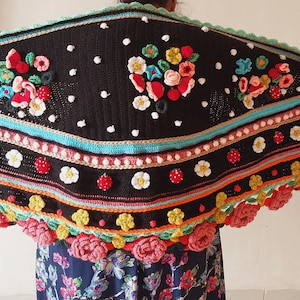 May include: A black crochet shawl with a colourful floral design. The shawl has a scalloped edge with large pink flowers and a border of smaller flowers and leaves. The shawl is decorated with white polka dots and a row of red strawberries.