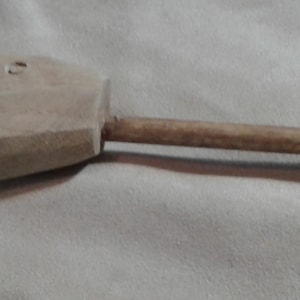 Op de afbeelding: Een houten gereedschap met een afgeronde kop en een lange, dunne steel. De kop heeft verschillende kleine gaten en de steel is gemaakt van lichtbruin hout.