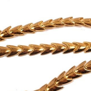 May include: A gold chain necklace with a chevron pattern. The chain is made of small, interlocking links that form a series of pointed triangles.