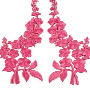 Könnte beinhalten: Zwei rosa gestickte Blumenapplikationen mit einem zarten Design. Jede Applikation zeigt eine Ansammlung von Blumen und Blättern, perfekt, um Kleidung oder Bastelarbeiten einen Hauch von Eleganz zu verleihen.