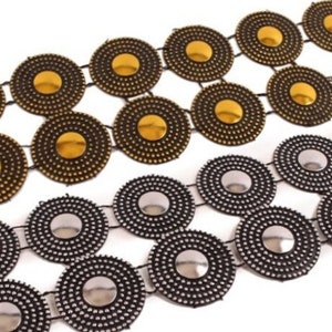 May include: Close-up of two decorative belts. One belt features gold-colored circular accents, while the other has silver-colored circular accents. Both belts have a black mesh backing and are displayed against a white background.