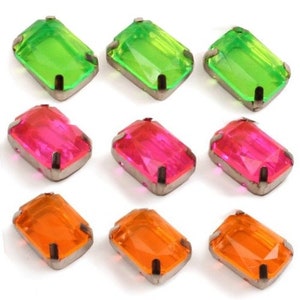 Könnte beinhalten: Neun smaragd-förmige, facettierte Glas-Strasssteine mit silbernen Fassungen. Die Strasssteine sind in drei Farben: grün, rosa und orange.