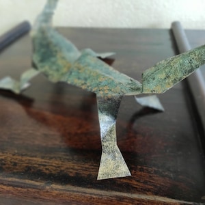 Könnte beinhalten: Eine grüne und goldene Origami-Skorpionskulptur auf einer dunklen Holzoberfläche.