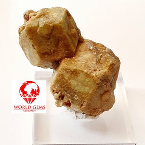 May include: A rough, golden-brown Grossular Garnet specimen from Kayé, Mali, displayed on a clear acrylic stand. The mineral's surface has a textured appearance. The label reads "Grenat Grossulaire Kayé, Mali."