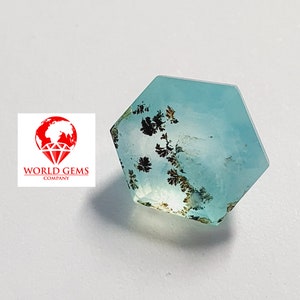 May include: A light blue gemstone with a hexagonal shape and black dendritic inclusions. The gemstone is cut and polished.