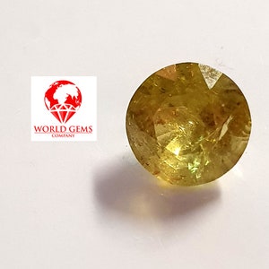 May include: A round, faceted, yellow gemstone with a slight green hue. The gemstone is set against a white background.