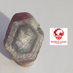 May include: A rough, hexagonal, gray and pink gemstone with a layered, striated pattern.  The gemstone is on a white background.