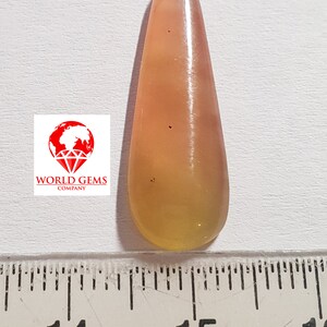 May include: A teardrop-shaped, translucent gemstone pendant with a yellow and orange colour gradient. The pendant is approximately 3.8 cm long and is measured against a ruler.