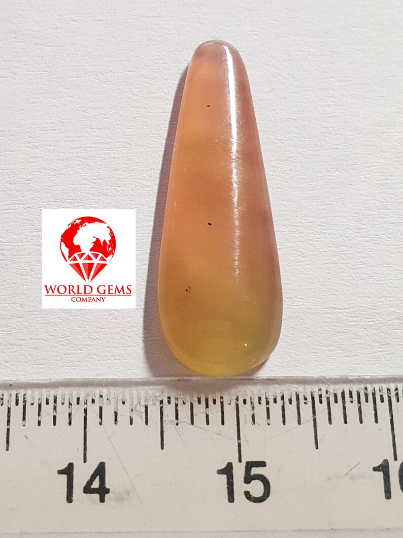 May include: A teardrop-shaped, translucent gemstone pendant with a yellow and orange colour gradient. The pendant is approximately 3.8 cm long and is measured against a ruler.