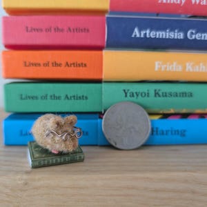 Needle felt mouse wearing spectacles sat on top of a book. With a background of books. Miniature mouse gift.
