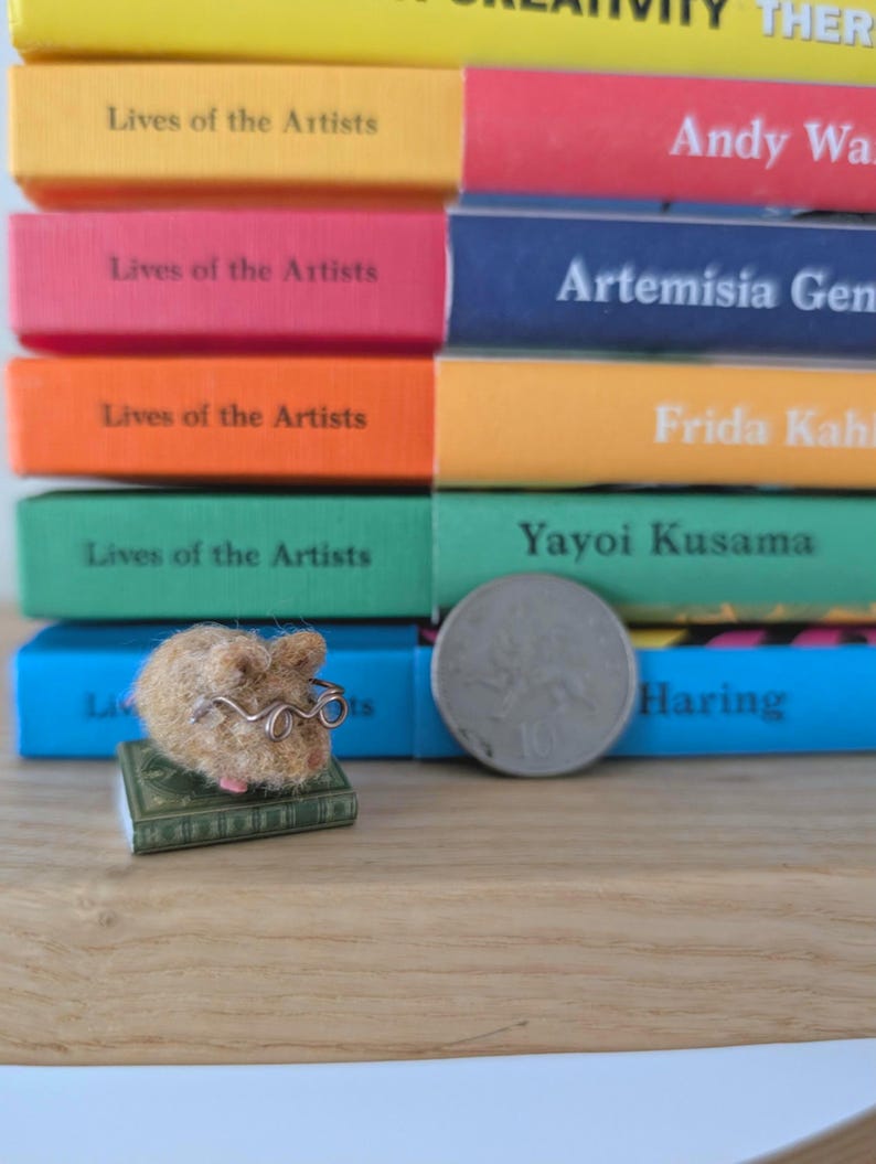 Needle felt mouse wearing spectacles sat on top of a book. With a background of books. Miniature mouse gift.