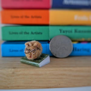 Needle felt mouse wearing spectacles sat on top of a book. With a background of books. Miniature mouse gift.