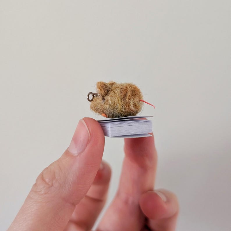 A persons fingers holding a Needle felt mouse wearing spectacles sat on top of a book. Miniature mouse gift suitable for book lovers.