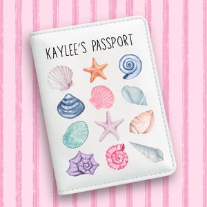May include: White passport holder with the text "KAYLEE'S PASSPORT" and watercolor illustrations of seashells and starfish in various colors. The background is a pink striped pattern.