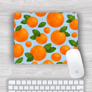 Puede incluir: Una alfombrilla de ratón rectangular con un fondo azul claro que presenta un patrón de naranjas naranjas con hojas verdes. Un ratón de ordenador blanco y un teclado blanco están en primer plano.