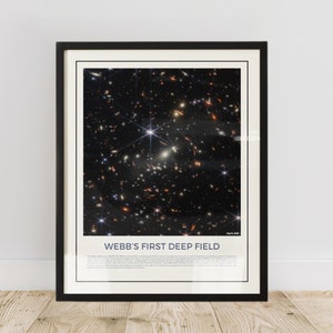 May include: A black framed poster with a photograph of a deep space field taken by the James Webb Space Telescope. The poster has the text "WEBB'S FIRST DEEP FIELD" and the date "July 12, 2022".