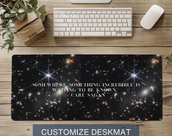 May include: A rectangular desk mat featuring a deep space image with stars and galaxies. The mat has a quote by Carl Sagan: "SOMEWHERE, SOMETHING INCREDIBLE IS WAITING TO BE KNOWN." The bottom of the mat reads "CUSTOMIZE DESKMAT YOUR FAVORITE QUOTE."