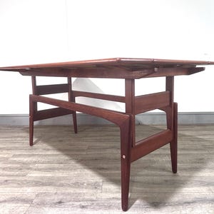 May include: A rectangular wooden dining table with a warm brown finish. The table features a flat top surface supported by a structural frame with four tapered legs and horizontal crossbars connecting the legs on each side of the furniture piece.