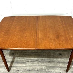 May include: A mid-century modern wooden dining table with a rectangular top and angled legs. The table is made of a light brown wood with a visible wood grain. The table is approximately 152 cm long and 91 cm wide.