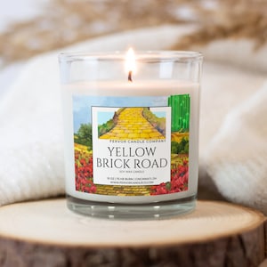 May include: A yellow soy wax candle with a label that reads "Fervor Candle Company Yellow Brick Road Soy Wax Candle 10 oz 175 hr burn | Cincinnati OH www.fervorcandleco.com". The label features a watercolor illustration of the yellow brick road from the Wizard of Oz.