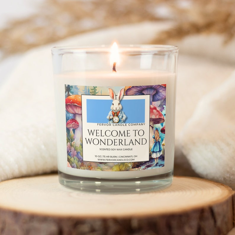 May include: A white soy wax candle in a clear glass jar with a label that says "Fervor Candle Company" and "Welcome to Wonderland". The label features a whimsical illustration of a white rabbit wearing a waistcoat and holding a pocket watch, surrounded by mushrooms and flowers.