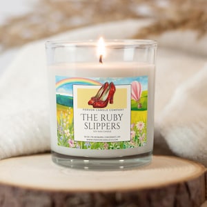May include: A lit soy wax candle in a clear glass jar. The label features a rainbow, red high-heeled shoes, and a hot air balloon. Text on the label reads "The Ruby Slippers" and "Fervor Candle Company."