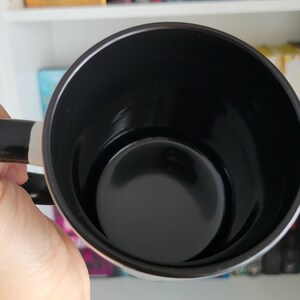 **ALT Text for Etsy Listing Image:**  
Close-up of a black-handled coffee mug with a glossy black interior, held by a hand against a bookshelf filled with romantasy and dark romance books. The smooth ceramic finish highlights the high-quality craftsmanship. Perfect for book lovers, fantasy readers, and coffee enthusiasts looking for a stylish and unique mug. Ideal for gifting or personal use.