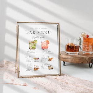 May include: A gold-framed sign with a white background and black text that reads "BAR MENU" with a list of drinks and their ingredients. The sign is on a pink surface.