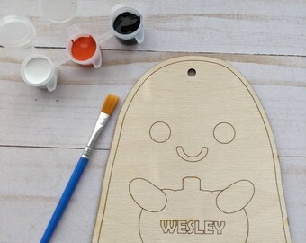May include: A wooden ghost cutout with a pumpkin and the name "WESLEY" inside. The ghost has two eyes and a smiling mouth. The cutout is ready to be painted with the included white, black, orange, and blue paint.
