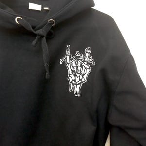 May include: Black hooded sweatshirt with a white skeleton hand graphic and the text "Pops & Fills" on the front.