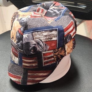 May include: A patterned baseball cap featuring a patchwork design with images of dogs and American flags. The cap's colors include red, white, blue, and various shades of brown and black. The cap is resting on a white form.