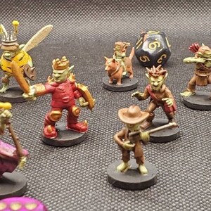 May include: A collection of miniature fantasy figures, including goblins and other creatures, are arranged on a dark surface. The figures are painted in various colors and poses, with some holding weapons and others with bows and arrows. Dice are also present.