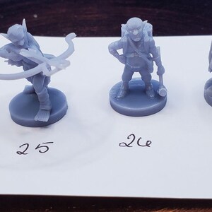 May include: Six gray miniature fantasy figures on round bases. The figures are of a goblin-like character in various poses, including one with a bow and arrow, and another with a backpack. Numbers 23 through 28 are written below each figure.