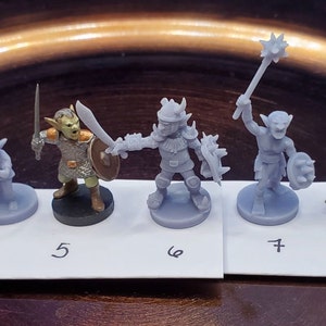 May include: A collection of miniature fantasy figurines, each depicting a different character. The figures are primarily gray, with some featuring painted details. The characters include warriors, archers, and other fantasy creatures. The figurines are arranged on a white surface.