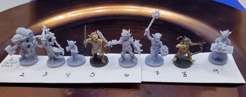 May include: A collection of miniature fantasy figurines, each depicting a different character. The figures are primarily gray, with some featuring painted details. The characters include warriors, archers, and other fantasy creatures. The figurines are arranged on a white surface.