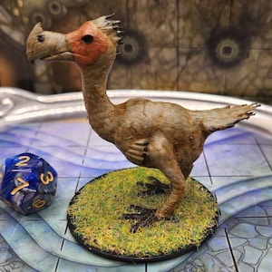 May include: A hand-painted miniature of a brown and white bird with a long beak and a tuft of feathers on its head. The bird is standing on a base covered in green grass.