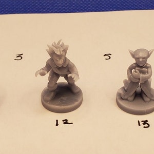 May include: A collection of gray miniature fantasy figures, each on a circular base. The figures include a warrior with a sword and shield, a wizard with a staff, and other characters. Numbers are written below each figure.