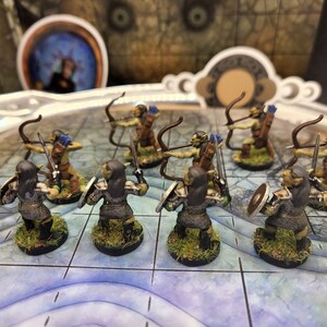 May include: Miniature fantasy figures of orcs, some with bows and arrows, others with swords and shields. The orcs are painted in shades of green, brown, and gray, standing on bases with grass. The figures are arranged on a blue and white grid.