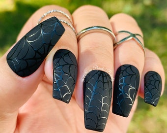 May include: Black long coffin-shaped false nails with a spiderweb design.