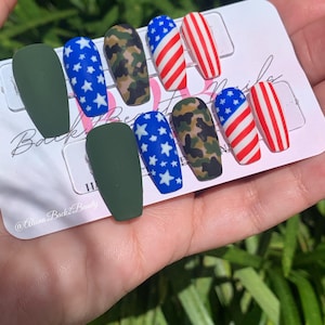 Puede incluir: Conjunto de diez u&ntilde;as postizas con tem&aacute;tica patri&oacute;tica. Las u&ntilde;as presentan un dise&ntilde;o verde, camuflaje, azul con estrellas blancas y bandera estadounidense roja, blanca y azul.