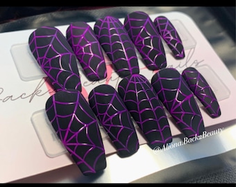 May include: Set of ten black press-on nails with a spiderweb design in purple. The nails are long and coffin shaped.
