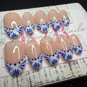May include: A set of oval-shaped false nails with a nude base and a blue and white floral design. The nails are arranged on a card that reads "Beauty Nails".