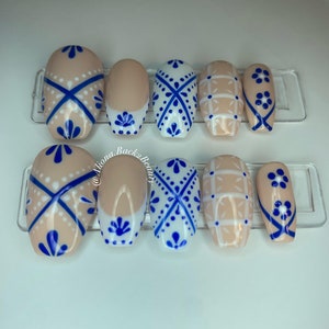 Puede incluir: Conjunto de diez uñas postizas con base blanca y diseños geométricos azules y blancos. Los diseños incluyen un patrón de cruz, un patrón de cuadrícula y un patrón floral.