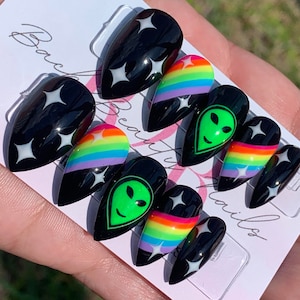 May include: Set of black press-on nails with rainbow stripes, white stars, and green alien faces.