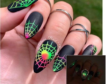 Op de afbeelding: Zwarte nagels met een neon groen, roze en geel spinnenwebontwerp. De nagels gloeien in het donker, zoals te zien is op de kleinere afbeelding.