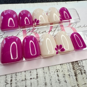May include: Two sets of press-on nails. Each set has a mix of solid magenta and off-white nails. The off-white nails have a magenta floral design. The nails are displayed on a white card with the text "Back Beauty Nails".